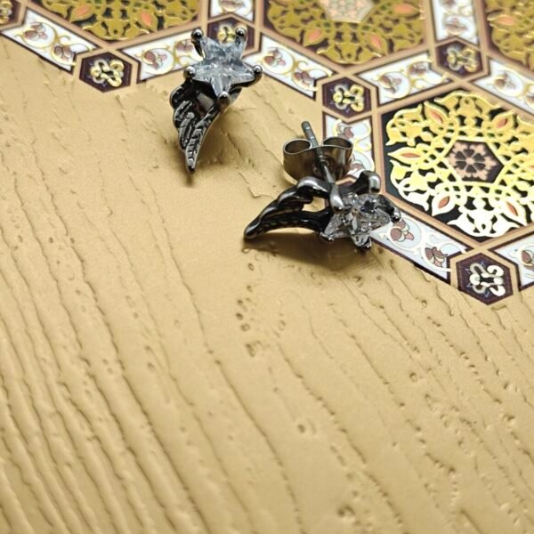 “Star wing stainless steel earrings with clear crystal stones on a light wood surface”