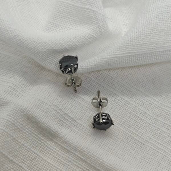 “Black stainless steel stud earrings with carved metal frame and dark stone on white surface”