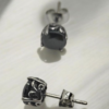 “Black stainless steel stud earrings with carved metal frame and dark stone on white surface”