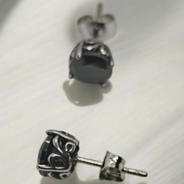 “Black stainless steel stud earrings with carved metal frame and dark stone on white surface”