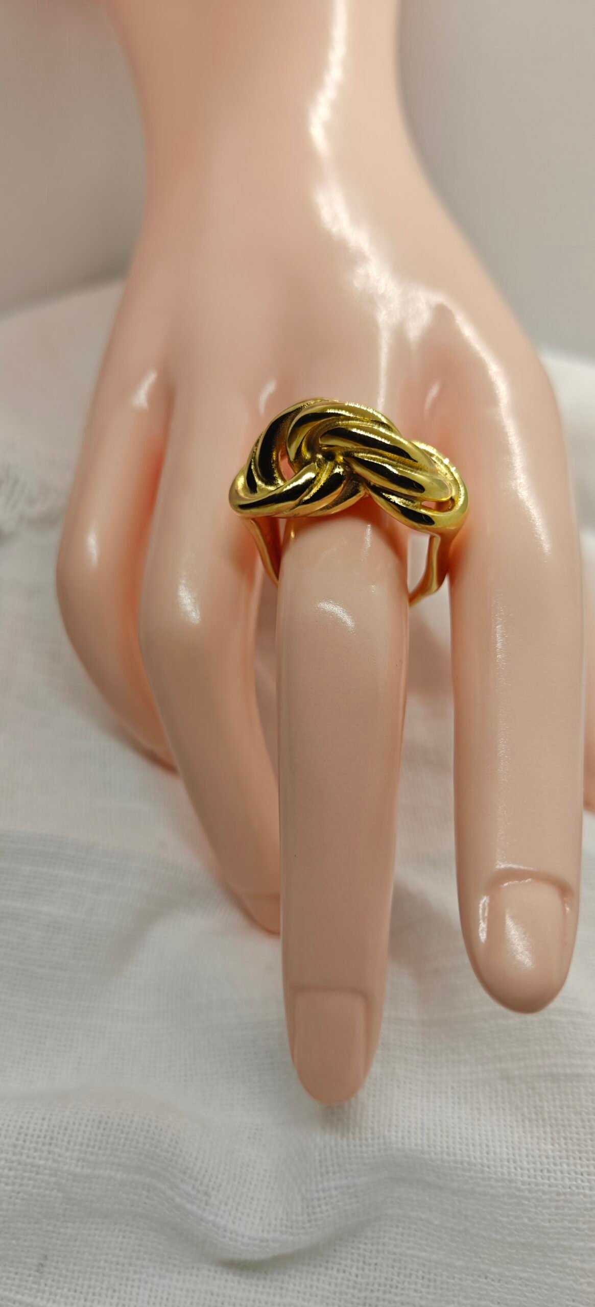 “A gold-plated stainless steel knot ring displayed on a mannequin hand over a white fabric background.”