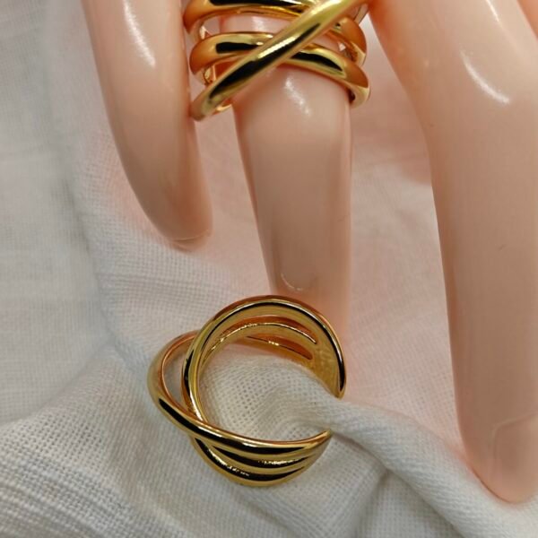 “Two gold-plated stainless steel crossover rings with interlocking band design displayed on white fabric.”