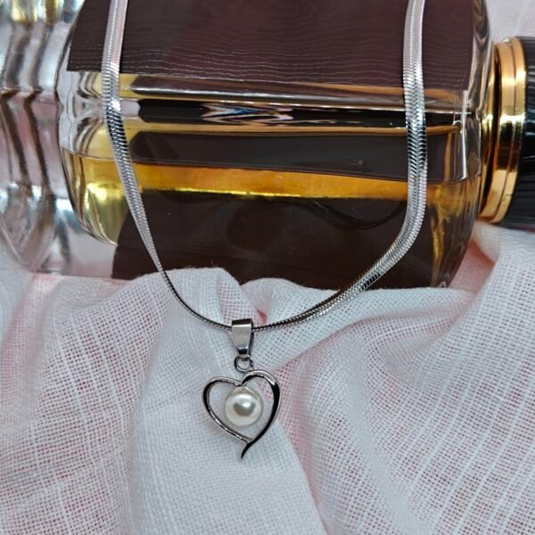 “Stainless steel heart pendant necklace with pearl center displayed on a white cloth backdrop.”