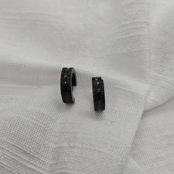 “Three pairs of small stainless steel hoop earrings in black finish displayed on a white fur surface.”