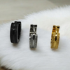 “Three pairs of small stainless steel hoop earrings in black, silver, and gold finishes displayed on a white fur surface.”