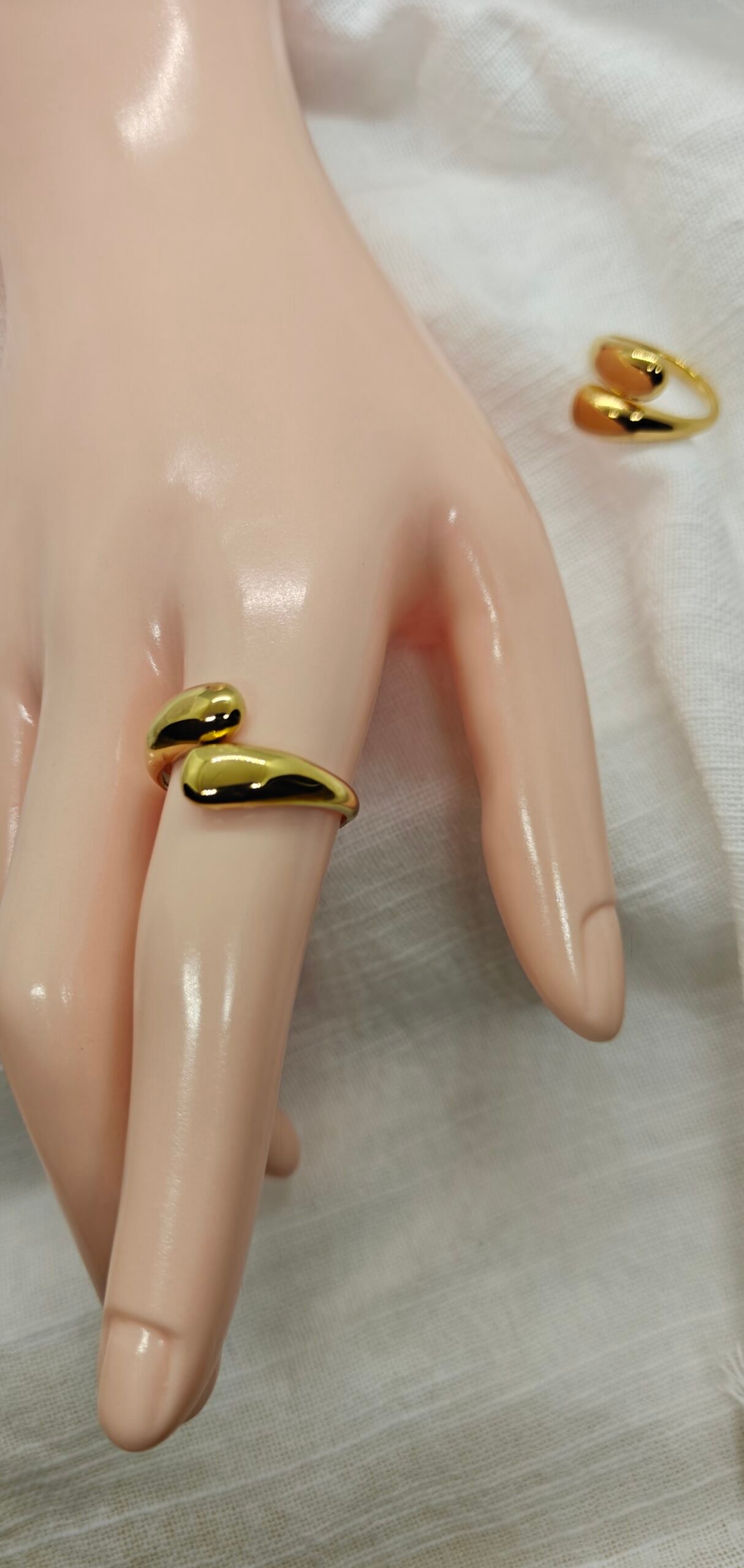 “Two gold-plated stainless steel rings with smooth fluid curves displayed on white fabric.”