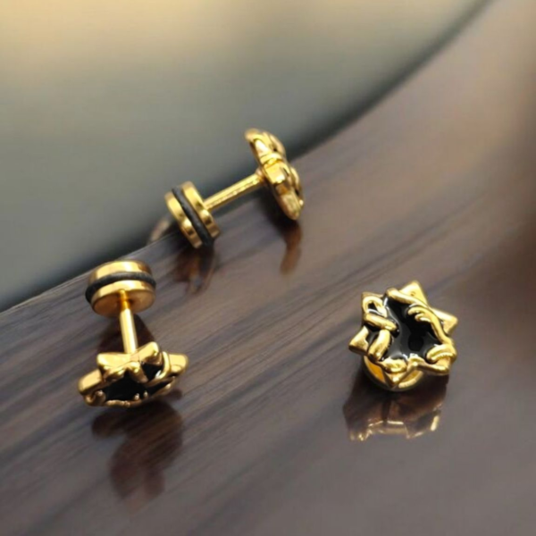 Gold-plated stainless steel star claw screw back earrings with black enamel accents on wooden surface