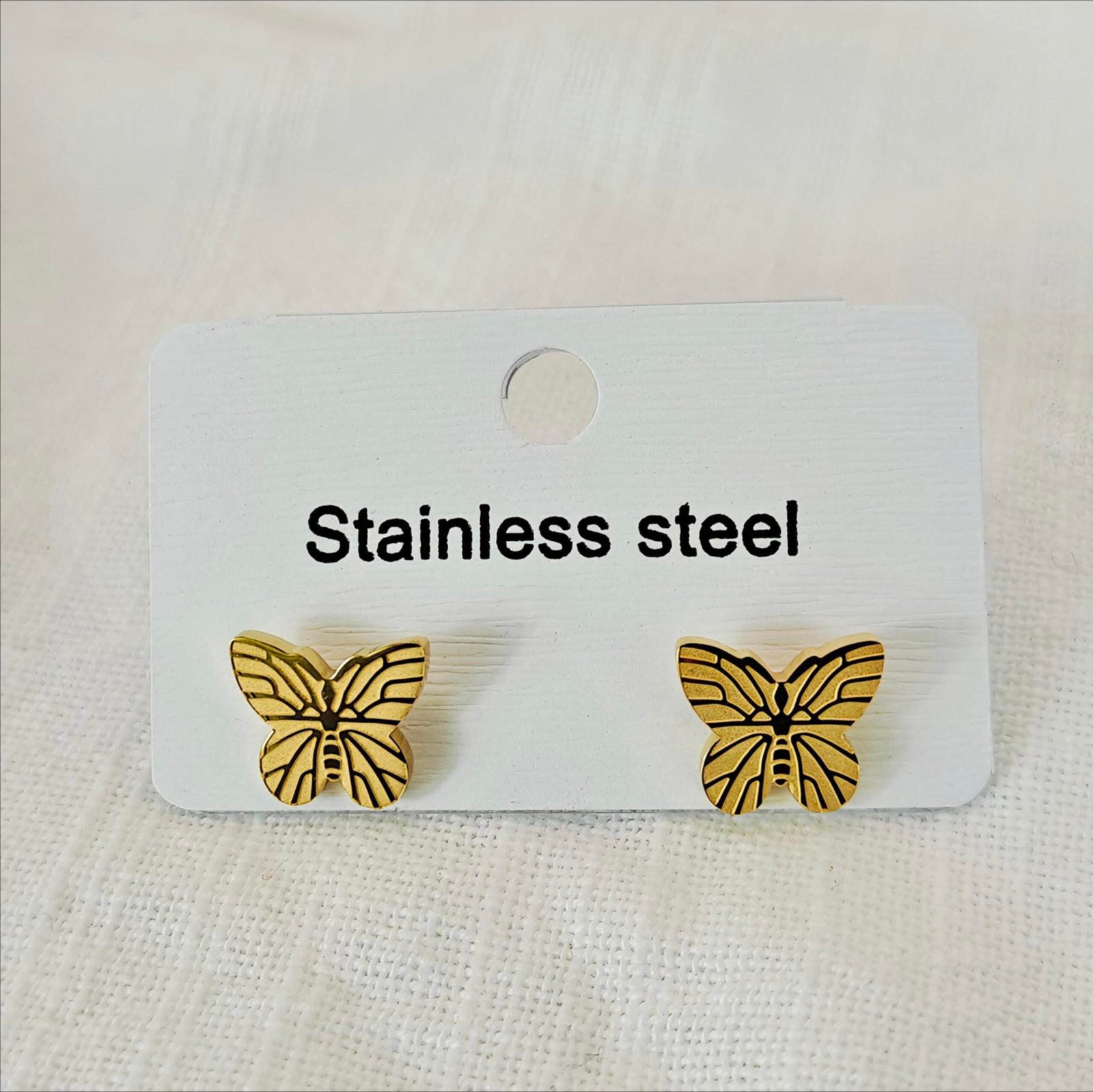 "HERDISE gold-tone butterfly stud earrings featuring symmetrical wings with black decorative detailing."
