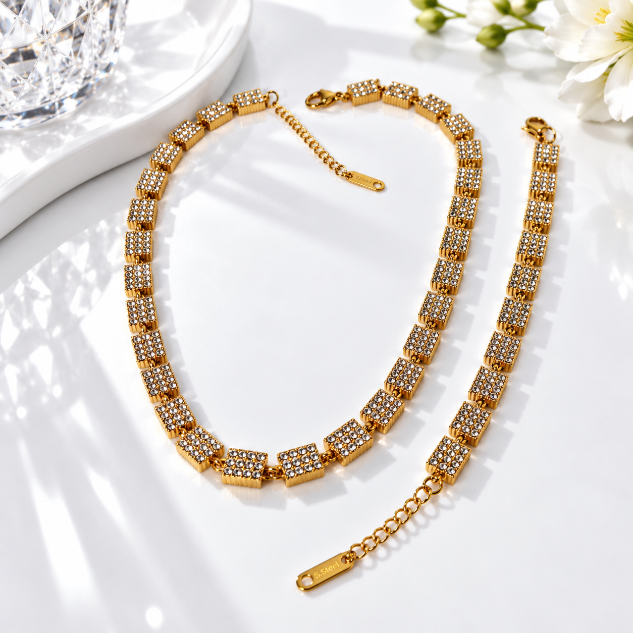 "HERDISE gold-tone rectangle crystal link necklace and matching bracelet displayed on a white surface with sparkling decorative accents."