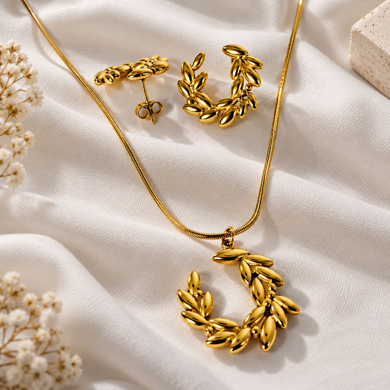 "HERDISE gold-tone olive branch necklace and matching earrings set displayed on soft white fabric."