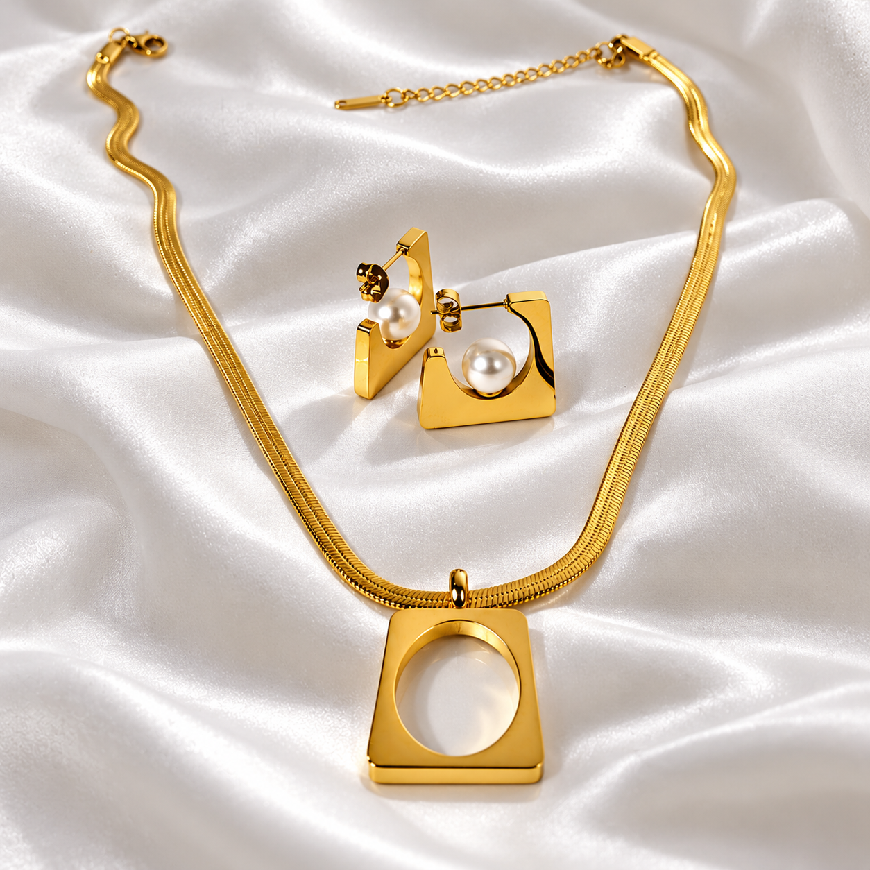 "HERDISE gold-tone geometric necklace and earrings set featuring a square pendant and pearl-style earrings on white satin."
